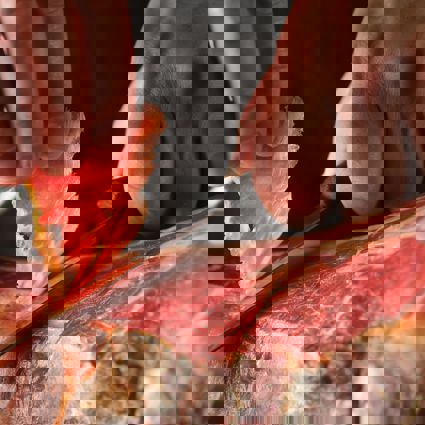 Person carving thin slices of meat from a jamon