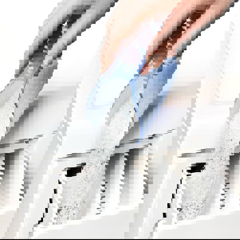 Person pouring a scoop of washing powder into a machine drawer