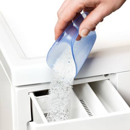 Person pouring a scoop of washing powder into a machine drawer