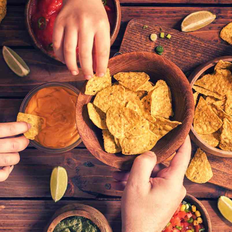 People sharing corn chips and dips