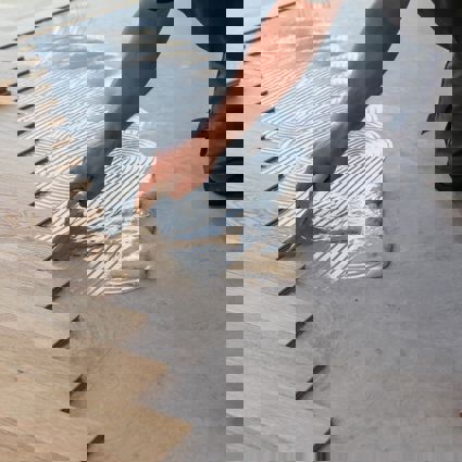 Person applying adhesive to floor to lay wooden flooring