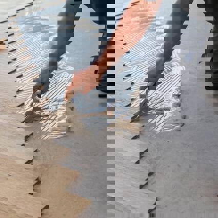 Person applying adhesive to floor to lay wooden flooring