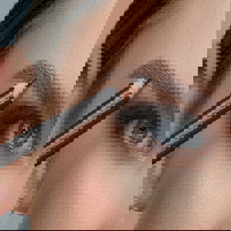 Person using a eyebrow pencil to define eyebrows 