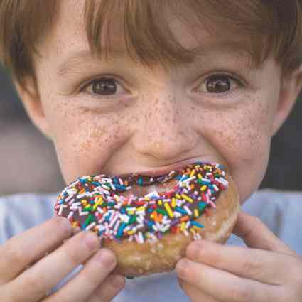 Boy biting into donut with sprinkles