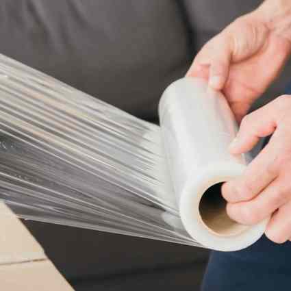 People stretching film over a cardboard box